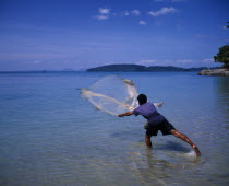 Ao Nang Beach.  Fisherman standing in shallows casting net into sea