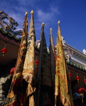 Chinese temple roof hung with red lanterns for Chinese New Year with richly embroidered flags in the foreground.