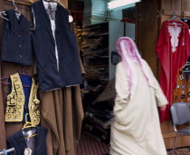Man in Dishdasha and red and white shmaaq entering clothes shop in the Great Souq in blurred movement. Store