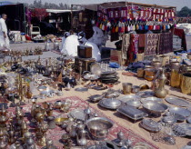 Brassware  crafts and textiles for sale at the Friday Market or souq with seated men wearing Dishdasha and Gutra.