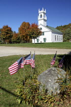 White wooden church and autumnal trees with American Stars & Stripes flags in the foreground.