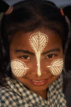 Head and shoulders portrait of young girl at U Bein Bridge near Mandalay wearing thanakha paste patterns on her face to beautify and protect skin from the sun.cosmetic made from tree bark. Burma Myan...