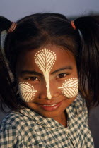 Head and shoulders portrait of young girl at U Bein Bridge near Mandalay wearing thanakha paste patterns on her face to beautify and protect skin from the sun.cosmetic made from tree bark. Burma