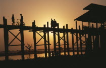 U Bein Bridge near Mandalay at sunset with silhouetted figures of monks  child and cyclist crossing.Burma Myanmar
