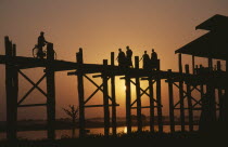 U Bein Bridge near Mandalay at sunset with silhouetted figures of monks and cyclist crossing.Burma Myanmar