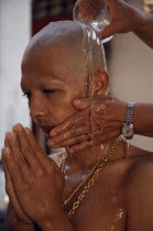 Novice monk having water poured over newly shaved head during ordination ceremony.