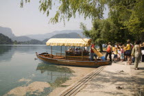 Tourists queuing to board one of the rowing boats for a trip to the island and church - the second boat has just arrived back  Pletnjaswooden rowing boatsrowerownerlarge oarsyellow striped canop...