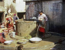 One of the villagers drawing water and others washing their hair at the village well in this Newari farming village in the Kathmandu Valley.  Metal water bucketswater bowlspouring waterladiesfem...