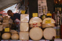 Market cheese stall with male stall holder displaying a selection of cheeses and euro money price signs