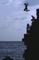 Arab boys climbing the old harbour walls to jump into the sea with a boy leaping into the air at the top