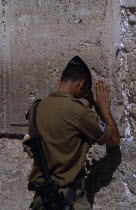 An Israeli Soldier in army uniform with an M16 Assault Riffle over his shoulder praying at The Western Wall Also known as The Wailing Wall