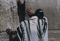 A Jewish man wearing a traditional prayer shawl praying at The Western WallAlso known as The Wailing Wall