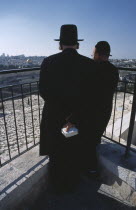 Two elderly Ultra Orthodox Jewish men one holding a bible in his hand surveying the cemetery on the Mount of Olives with the Old City in the background