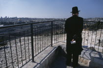 Elderly Ultra Orthodox Jewish man holding a bible in his hand surveying the cemetery on the Mount of Olives with the Old City in the background