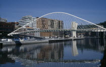 Campo Volantin footbridge over the River Nevion near the Guggenheim with high rise apartment buildings behind reflected in water below.