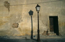 Street lamp casting shadow against cracked and peeling plaster wall.