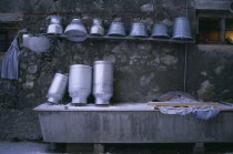 Washed milk churns and pails on shelf above trough.
