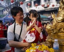 Man holding young girl in front of Buddha statue at Chinese New Year celebrations.prayer