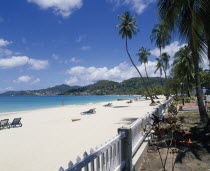 View along empty sandy beach towards turquoise sea and hills seen from across water