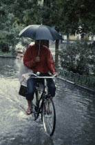 Cyclist riding through flooded street holding umbrella with one handFlood