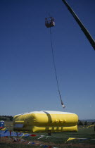 Bungee jumper suspended from crane over inflated safety mat.