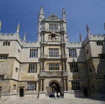 The Old Bodleian Library exterior facade with people walking through arched entrance to interior courtyard.