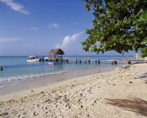 Sandy beach with boats at wooden jetty with tree leaves from right and foot prints in sand
