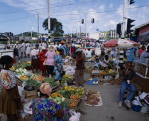 Fruit and  vegetable street market. Pumpkins  carrots  cabbage  yams  spring onions  bananas  oranges near street with traffic lights and ice-cream vendor in background.