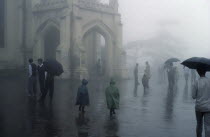 Monsoon rain falling in Simla India with people walking with umbrellas and children in coloured raincoats Colored