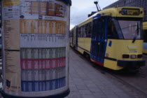 Sign detailing tram times with passing tram beyond.
