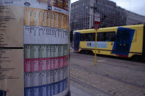 Sign detailing tram times with passing tram beyond.