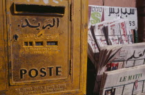 Close cropped view of postbox beside rack of French and Arabic newspapers.   Marrakesh