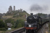 Corfe Castle seen behind a railway line with a steam train approachingGreat Britain United Kingdom UK