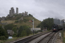 Corfe Castle seen behind a railway line with a steam train approachingGreat Britain United Kingdom UK