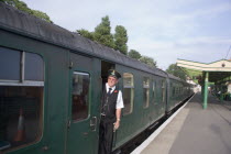 Steam Railway Station. View along platform with train departing from station and train conductor seen looking out from carriagesGreat Britain United Kingdom UK