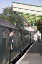 Steam Railway Station. View along platform with train departing from station and train conductor seen looking out from carriagesGreat Britain United Kingdom UK