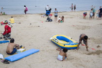 Sunbathers and children playing on sandy beach near inflatables and a dingy boatGreat Britain United Kingdom UK