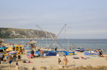 Busy colourful sandy beach scattered with inflatables and windbreaks and a bungee amusement ride next to a tiki hut in the middleGreat Britain United Kingdom Colorful UK