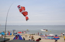Busy colourful sandy beach with sunbathers on the sand and speedboats on the sea. Fish kite blowing in the wind in the foreground.Great Britain United Kingdom Colorful UK