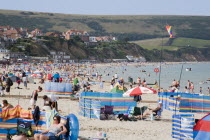 Sunbathers on busy sandy beach with colourful windbreaks and inflatables overlooked by hotelsGreat Britain United Kingdom Colorful UK