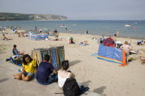 Busy sandy beach with sunbathers on the sand near deckchairs and windbreaks.Great Britain United Kingdom UK