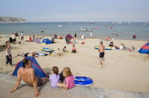 A man sat with small children looking out towards busy sandy beach with sunbathers on the sand and swimming in the seaGreat Britain United Kingdom UK