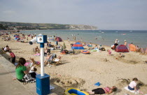 View across busy sandy beach with sunbathers on the sand towards the sea. Viewing telescope in the foreground.Great Britain United Kingdom UK