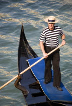 A gondolier in traditional dress of beribboned straw hat  striped vest and black trousers on his gondola