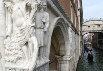 A 15th Century stone carving depicting the Drunkenness of Noah  symbolic of the frailty of man  on the corner of the Doges Palace. Gondolas pass along the Rio Del Palazzo under the Bridge of Sighs