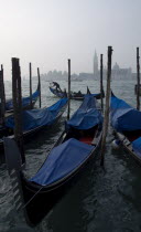 A gondolier works his gondola past others moored at the Molo San Marco with Palladios church of San Giorgio Maggiore on the island of the same name in the distance on a misty day