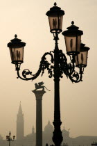 An ornate lamp post and the Column of Saint Mark in the Piazzetta with Palladios church of San Giorgio Maggiore on the island of the same name in the distance on a misty day