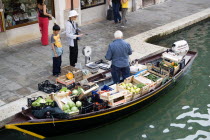 A fruit and vegetable vendor serving a customer from his boat moored alongside the Fondamenta dei Vetrai along the Rio dei Vetrai canal on the lagoon island of Murano
