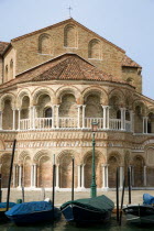 The colonnaded exterior of the Basilica dei Santa Maria e Donato with boats moored along the Canale di San Donato on the lagoon island of Murano