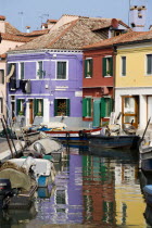 Colourful houses beside a canal on the lagoon island of Burano with boats moored alongside the edge of the canal. Colorful